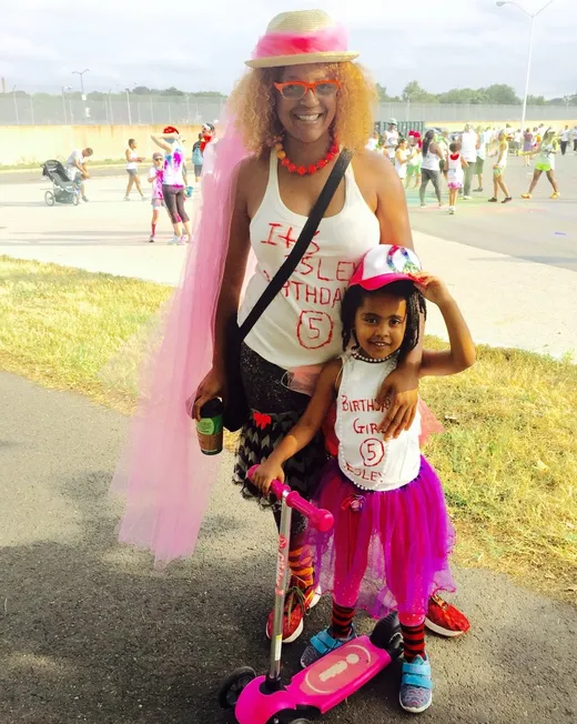 Tami in a pink hat and tutu with her young daughter at a festival